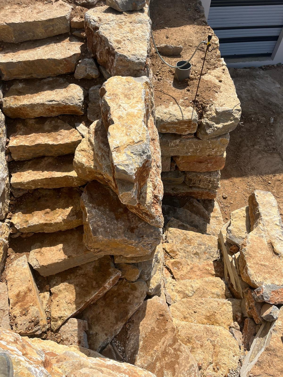Vue plongeante sur un escalier extérieur et un mur de soutènement en grandes pierres naturelles, entouré de terre meuble, illustrant un projet de terrassement.